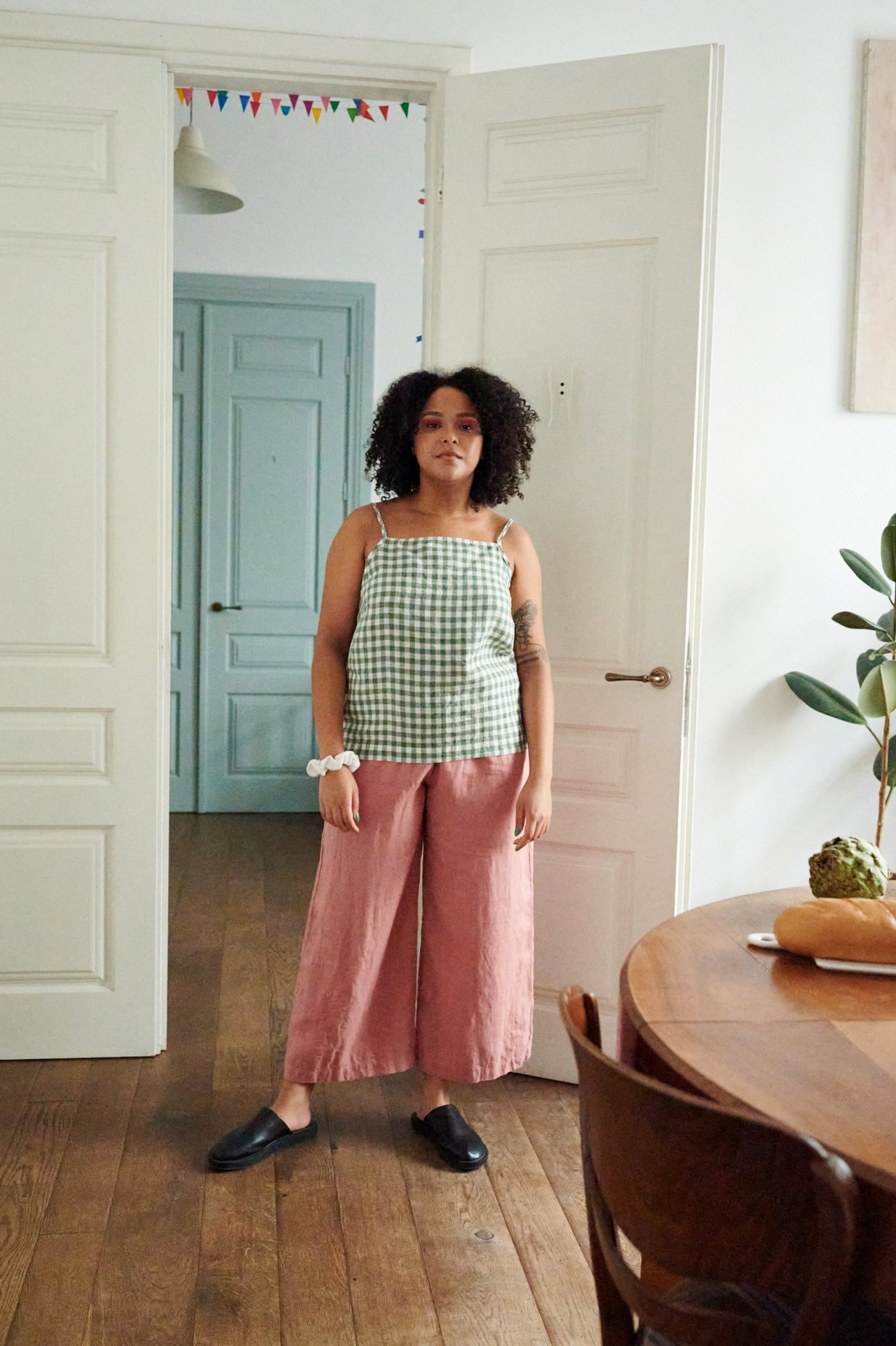 Woman wearing a green gingham linen top with thin straps and wide-leg cropped linen trousers