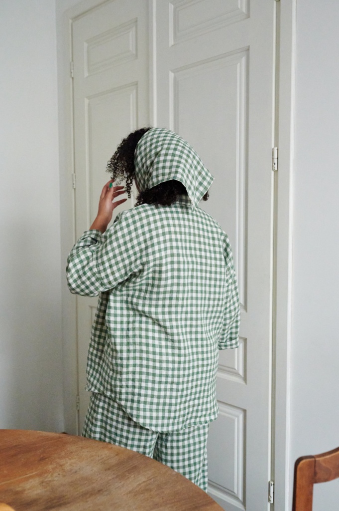 Back of a model wearing a green gingham linen button down shirt with rolled up sleeves