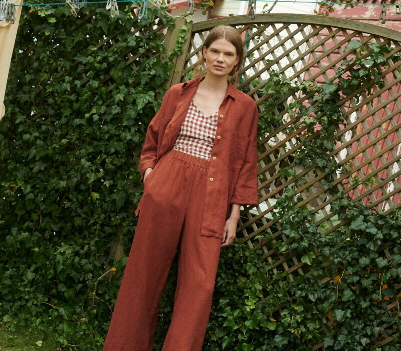 model in a garden wearing a terrracotta gingham linen wrap top and wide leg linen trousers and shirt in terracotta linen