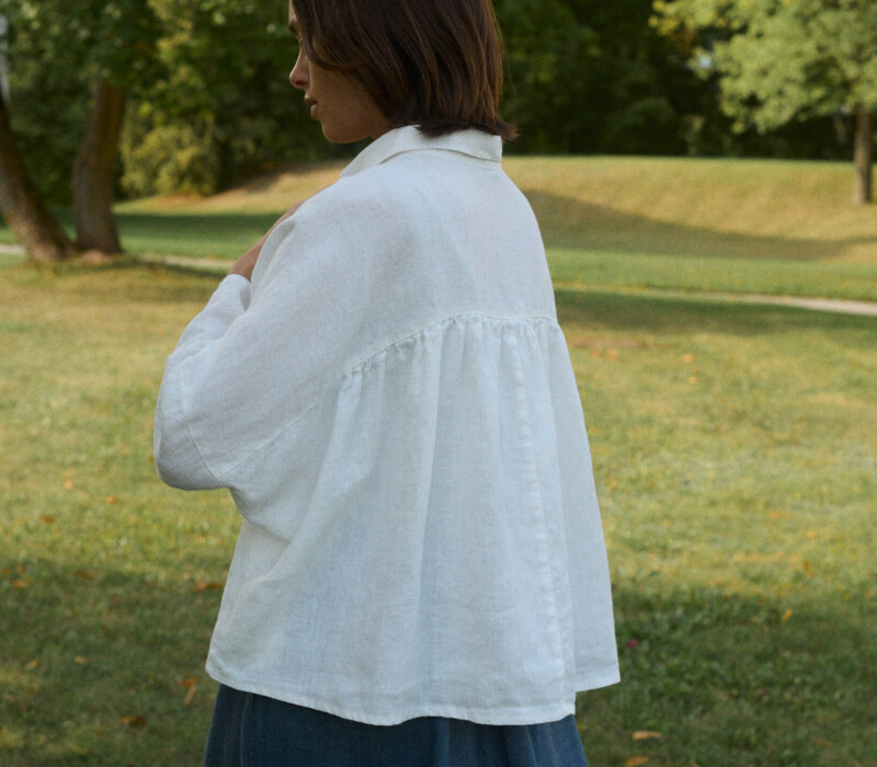 Woman wearing a flowy linen white top with ruffled back detail and a blue linen wool blend skirt