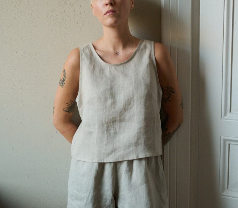 Model wearing a sleeveless top in natural grey linen with a rounded neckline and cropped length, paired with matching shorts, creating a relaxed loungewear look