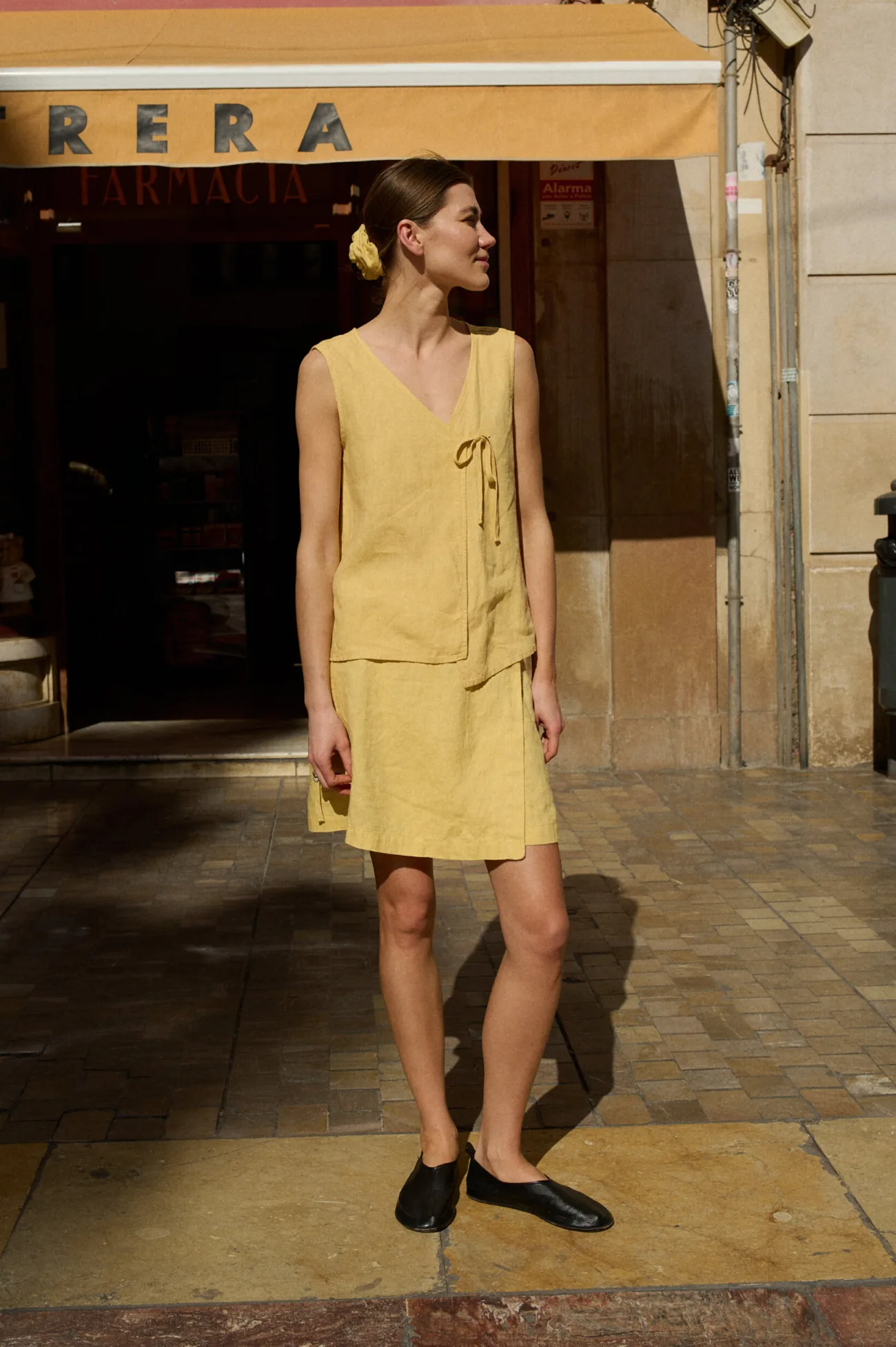 Model in a coordinated butter yellow linen outfit consisting of a sleeveless V-neck top with a side tie and a matching A-line wrap skirt