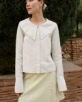 Model wearing a white cotton blend blouse with an oversized Peter Pan collar, button-down front, and full-length sleeves with subtle cuffs, paired with a pale apple checks linen wrap skirt featuring side tie closures and a subtle A-line shape
