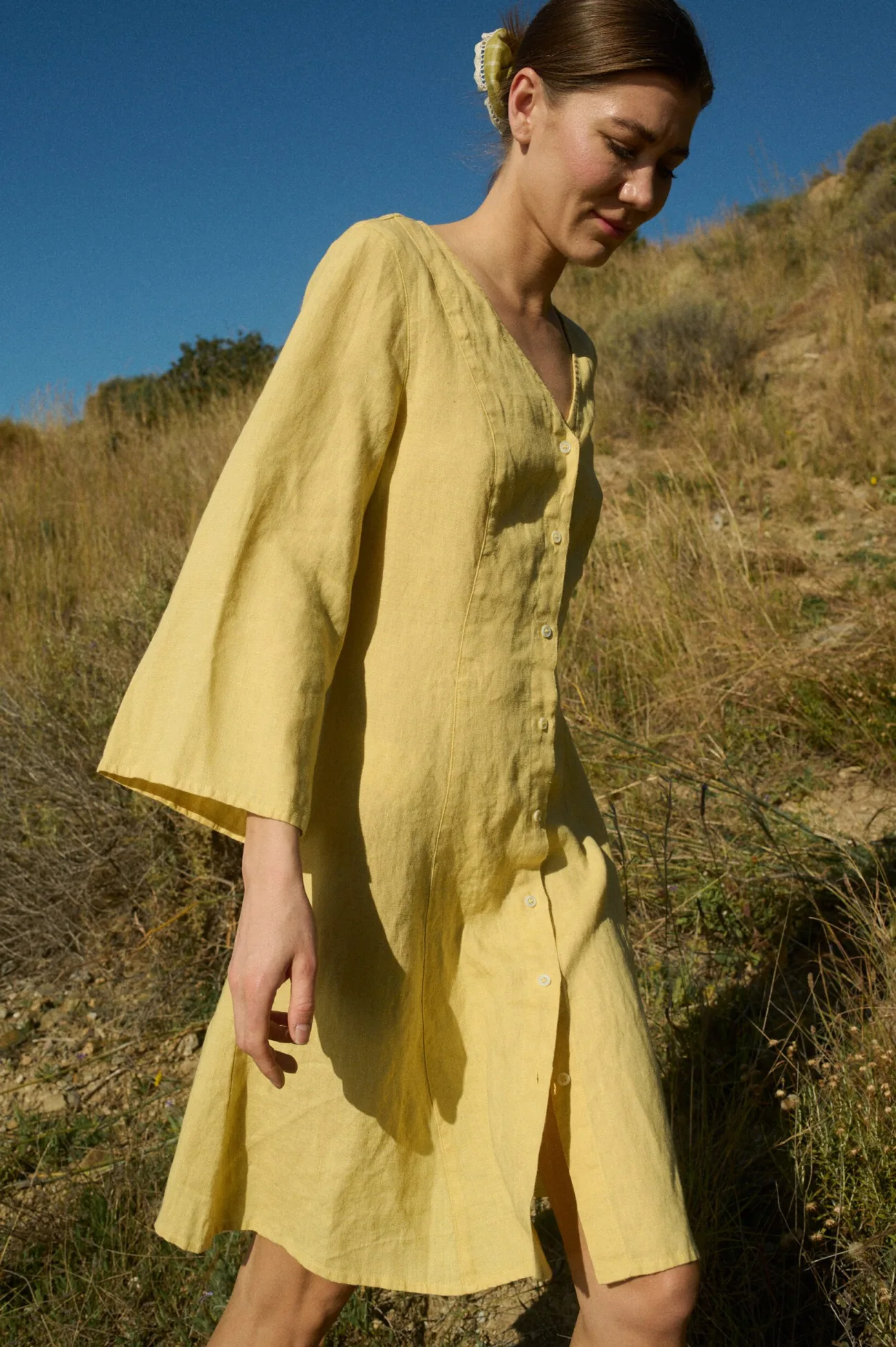 Model in a yellow linen dress with a V-neck, button-down front, ¾ flared sleeves, and a relaxed A-line silhouette, accented by vertical panels and godet inserts for added movement and shape