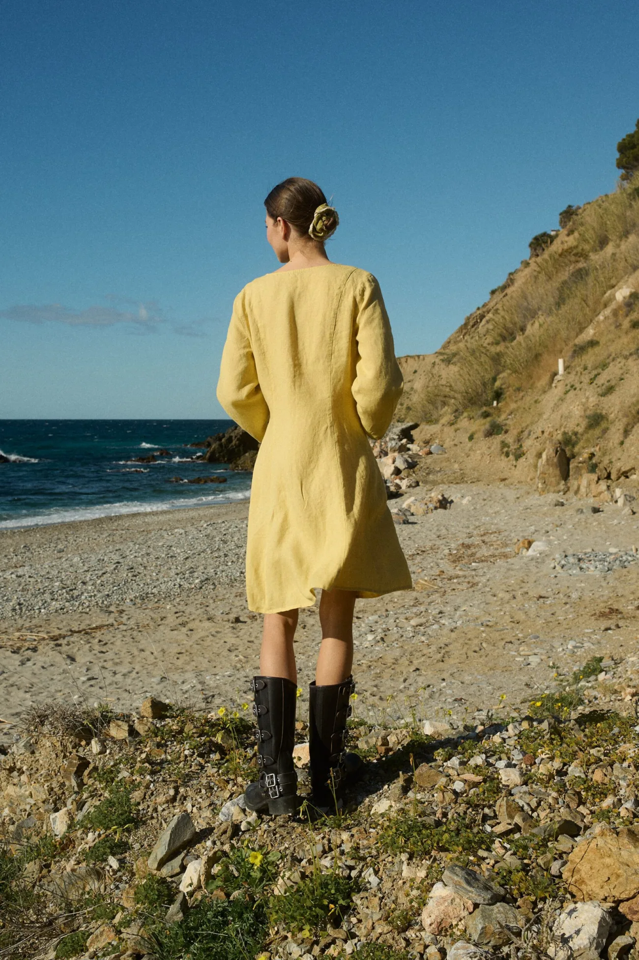 Model seen from the back in a yellow linen dress with a relaxed A-line fit and vertical panels