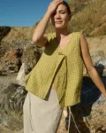 Model standing on rocky terrain, wearing a pickle checks linen sleeveless wrap top with a side tie, paired with a natural cotton blend skirt