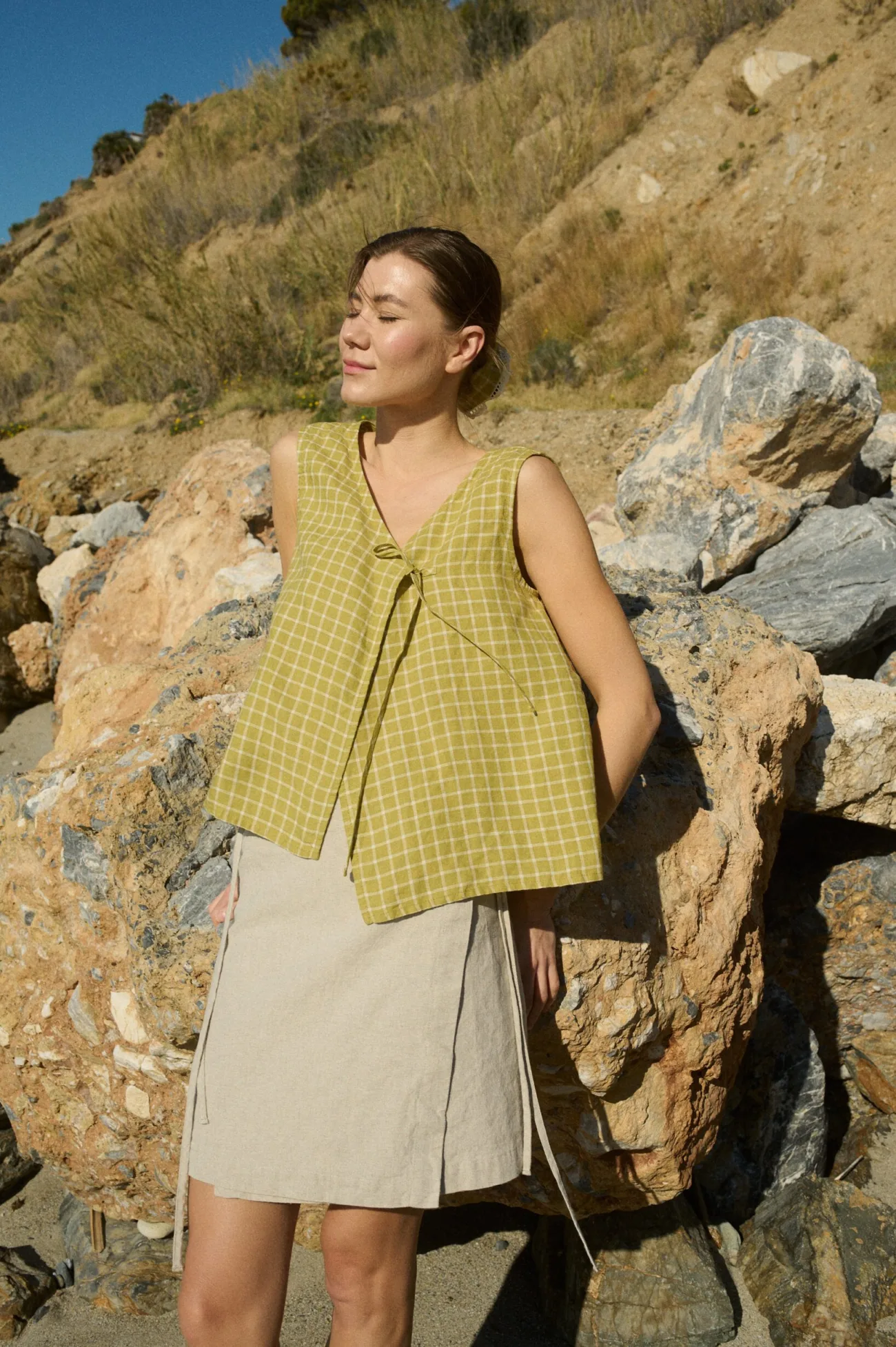 A sleeveless wrap top in pickle checks grid-patterned linen with a flattering side tie, offering a relaxed silhouette, paired with a natural-toned mini skirt made from a soft cotton blend