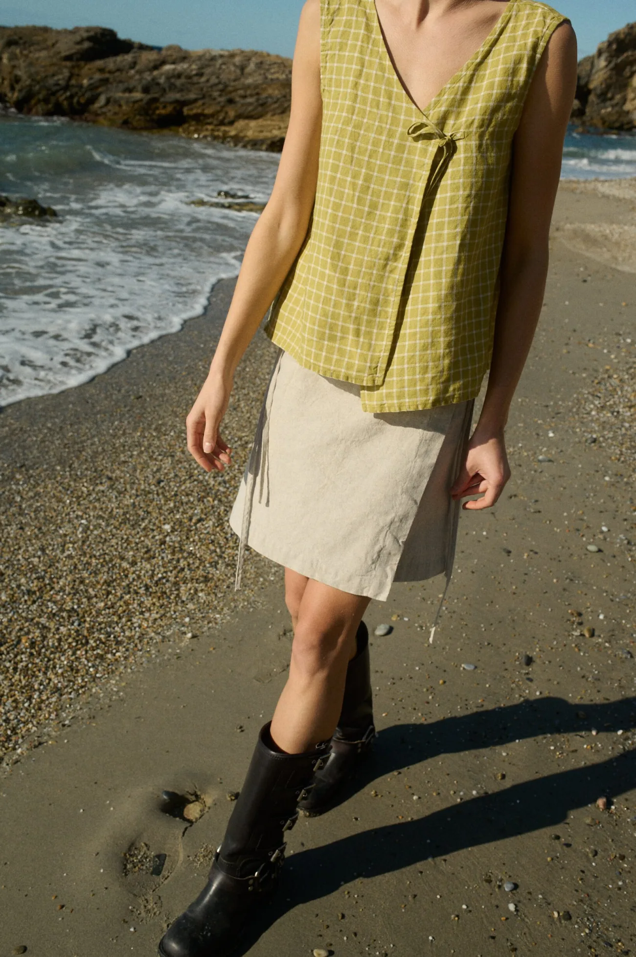 Model wearing a relaxed-fit sleeveless wrap top in pickle checks grid-patterned linen, paired with a linen and cotton blend wrap skirt in a clean, straight cut with a mini length and adjustable side ties