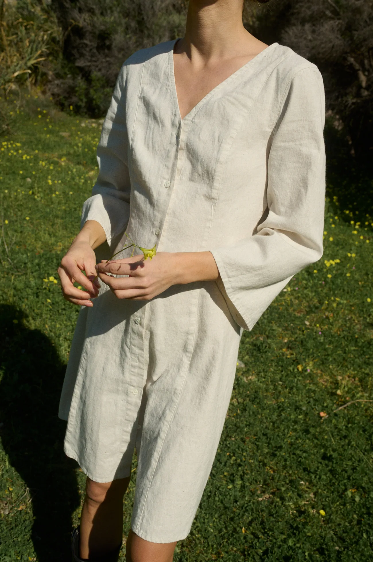 Model wearing a white cotton blend mini dress with a button-down front, V-neckline and three-quarter length sleeves that flare at the cuffs