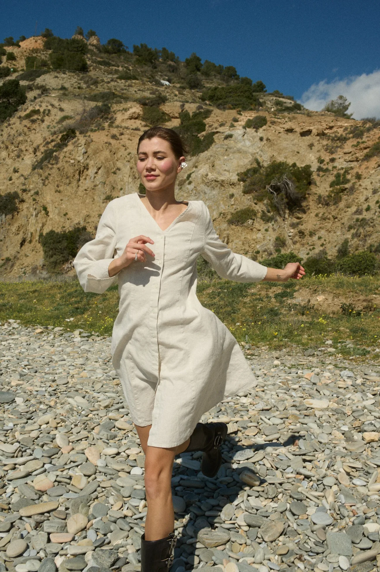 Model running a white cotton blend dress with a button-down front, V-neckline, three-quarter sleeves that flare at the cuffs, and an A-line silhouette that reaches knee length