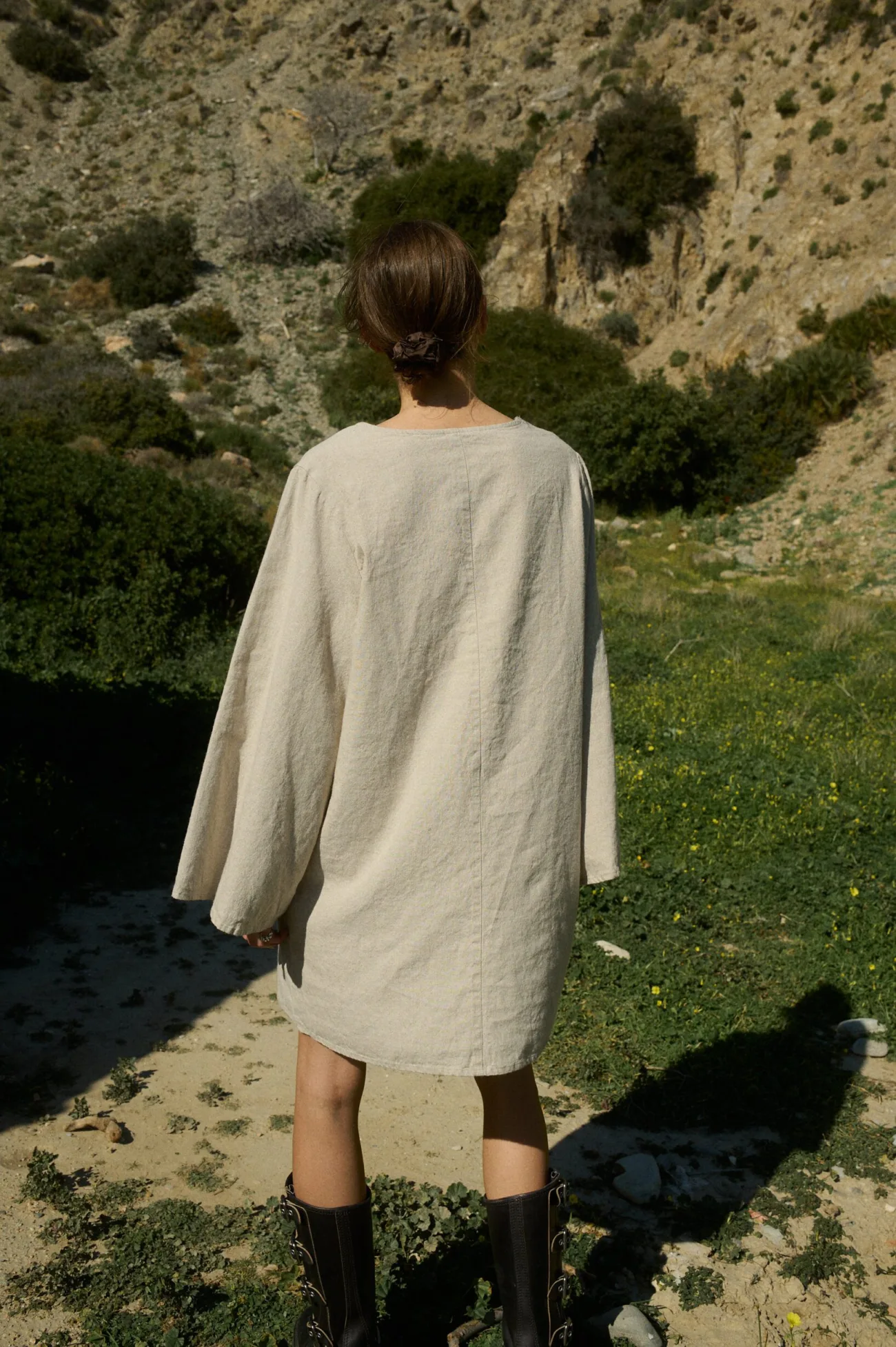Back view of a model wearing a mini length natural cotton blend dress with long flared sleeves