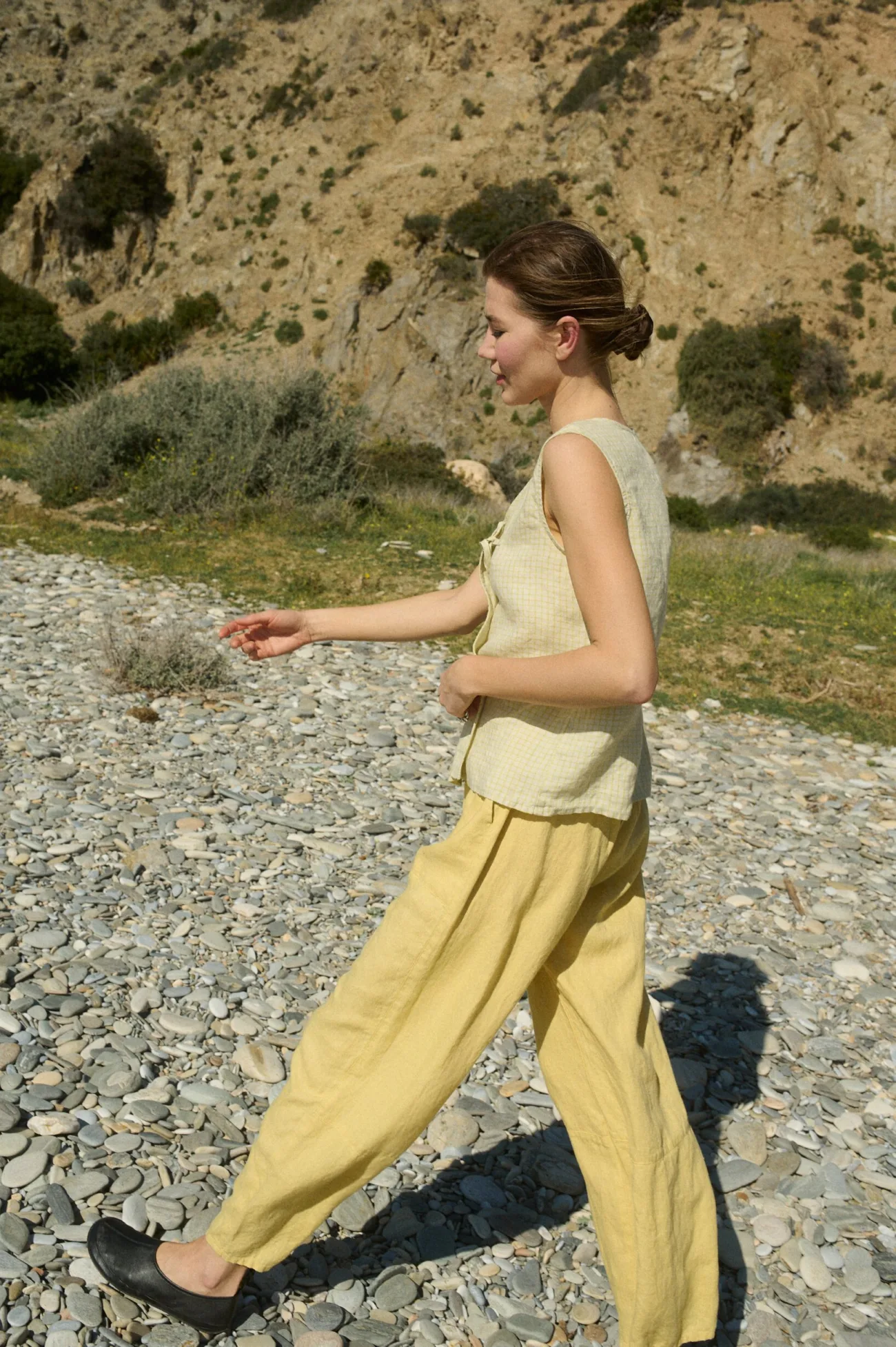Model walking in a pale yellow checkered sleeveless linen top with tie closure, paired with matching butter yellow wide-leg linen pants