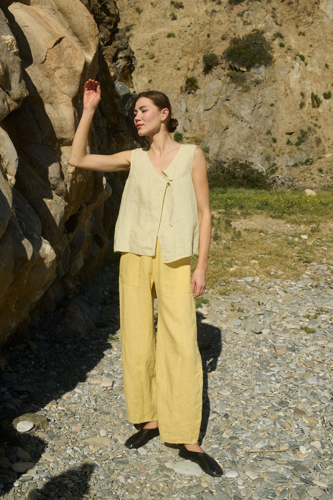 Model wearing a sleeveless V-neck top in airy apple checks linen, featuring a delicate side tie and a relaxed fit, paired with wide-leg butter yellow linen pants for a effortlessly coordinated look