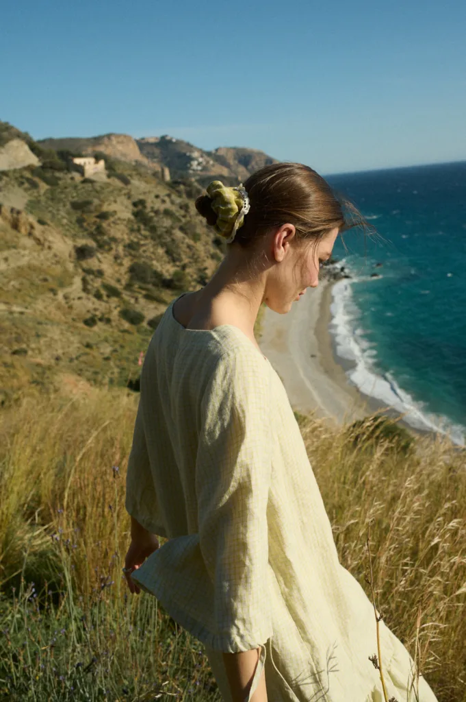 Woman wearing an apple checks linen dress with wide, relaxed sleeves, complemented by a linen hair scrunchie in pickle checks, adding a charming touch to her pulled-back bun