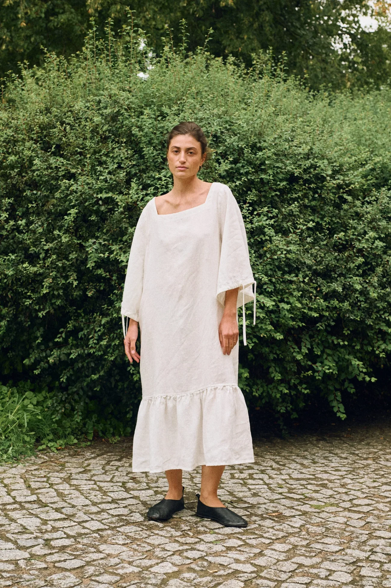 Milky white linen midi dress with wide sleeves and ruffle hem worn by a model outdoors