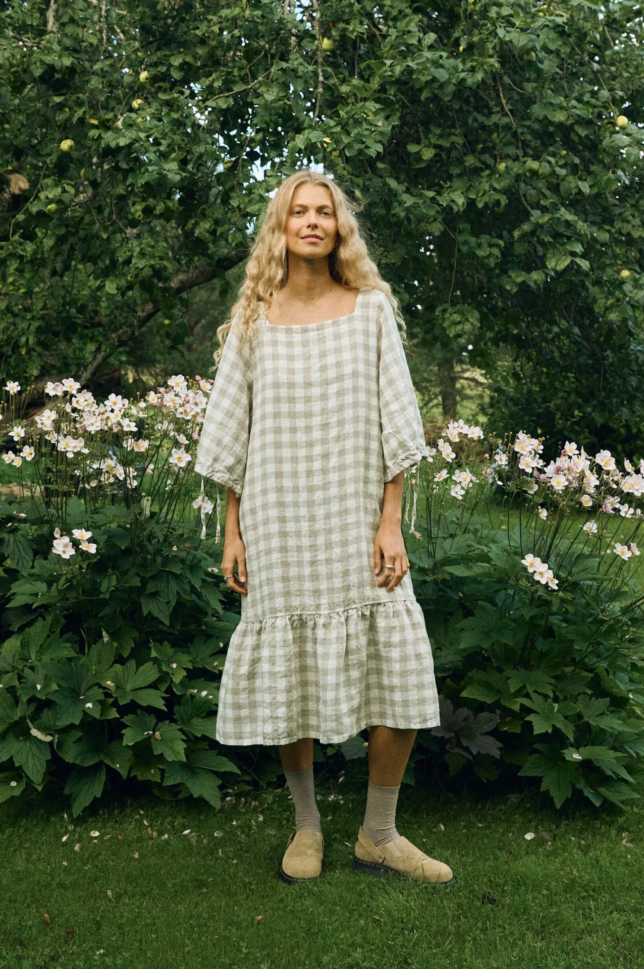 Front view of a relaxed, square-neck dress in large natural gingham linen, featuring elbow-length drawstring sleeves and a softly gathered ruffle hem