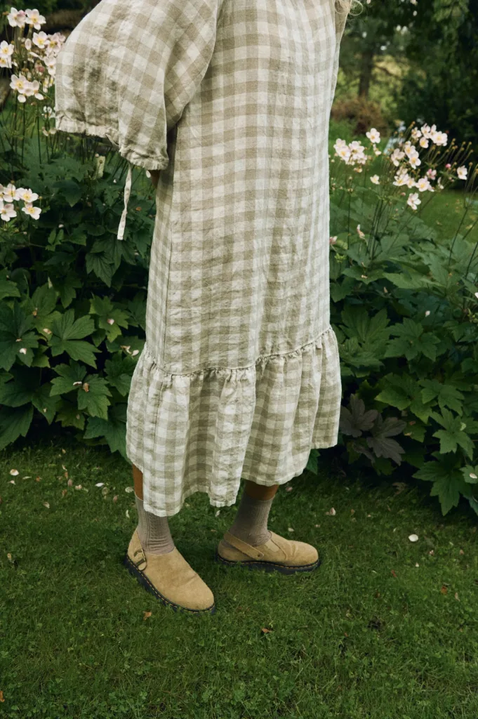 Close-up of the lower half of the dress in large natural gingham linen, highlighting the gathered ruffle hem and soft texture of the fabric