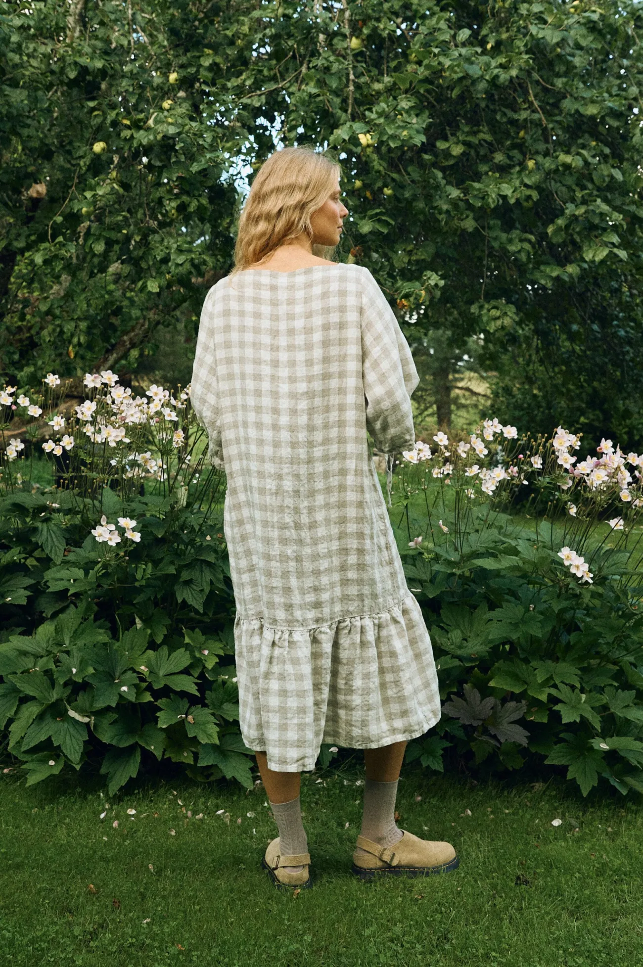 Back view of a relaxed-fit midi dress in large natural gingham linen, featuring dropped shoulders and a softly gathered ruffle hem