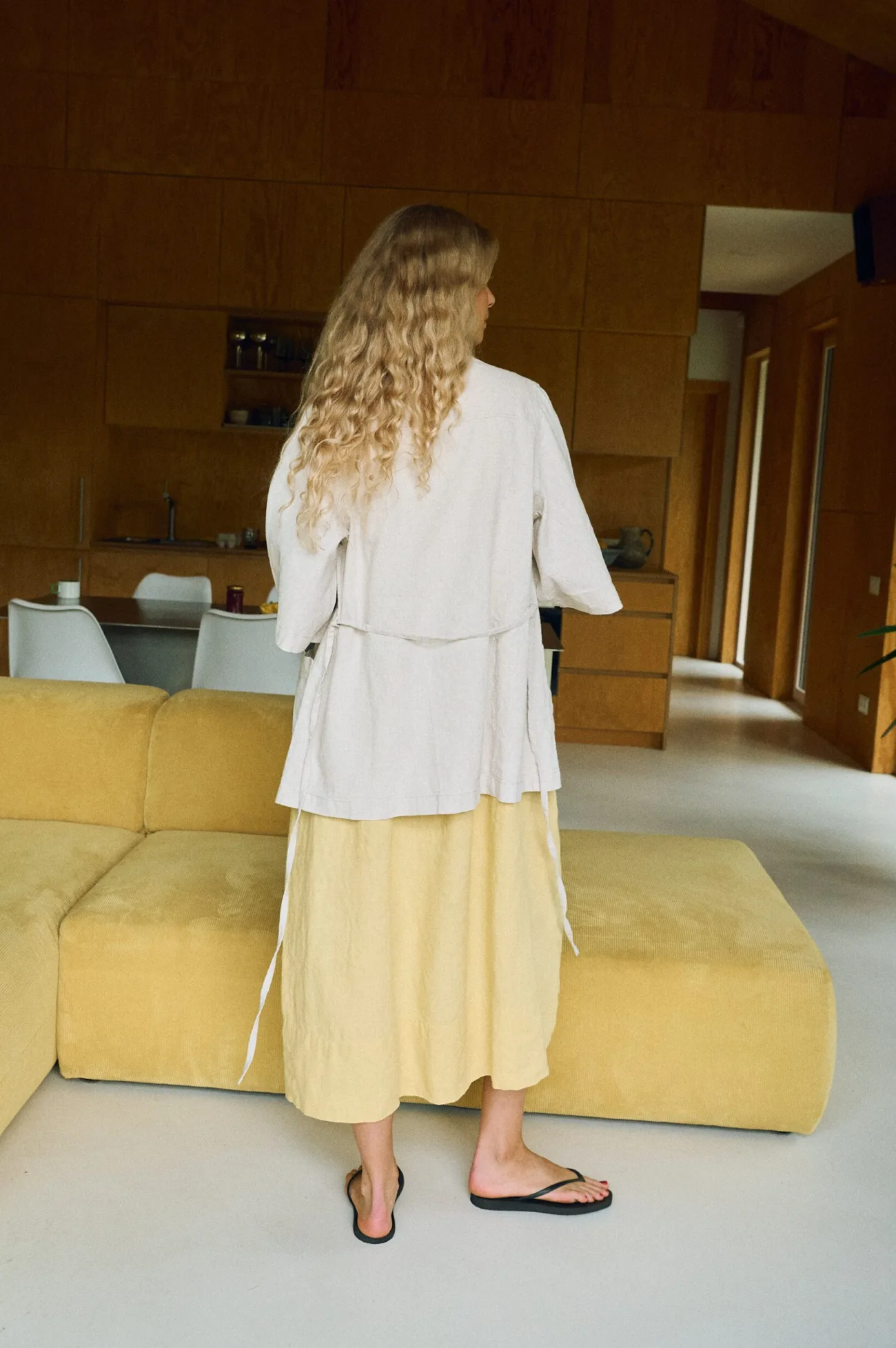 Back view of a laid-back linen ensemble featuring a light yellow sleeveless midi dress layered with a soft natural linen-cotton overshirt, complete with waist ties