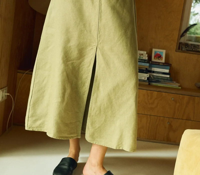 Close-up of a high-waisted olive green midi skirt made from heavy linen, featuring a front slit, belt loops, and a structured A-line cut