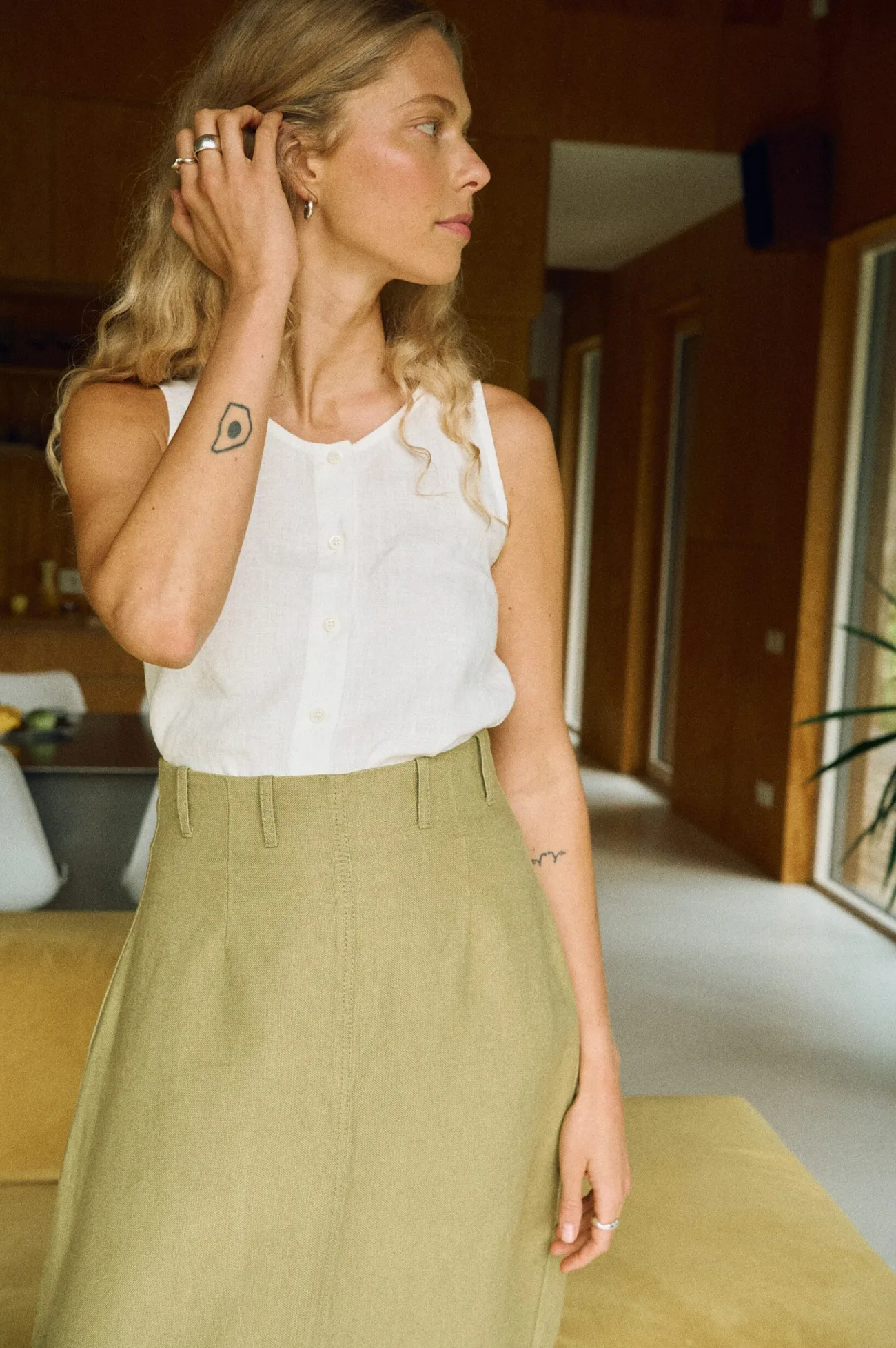 Close-up of woman wearing a sleeveless white linen button-up top tucked into a high-waisted olive green heavy linen skirt with belt loops and a structured fit
