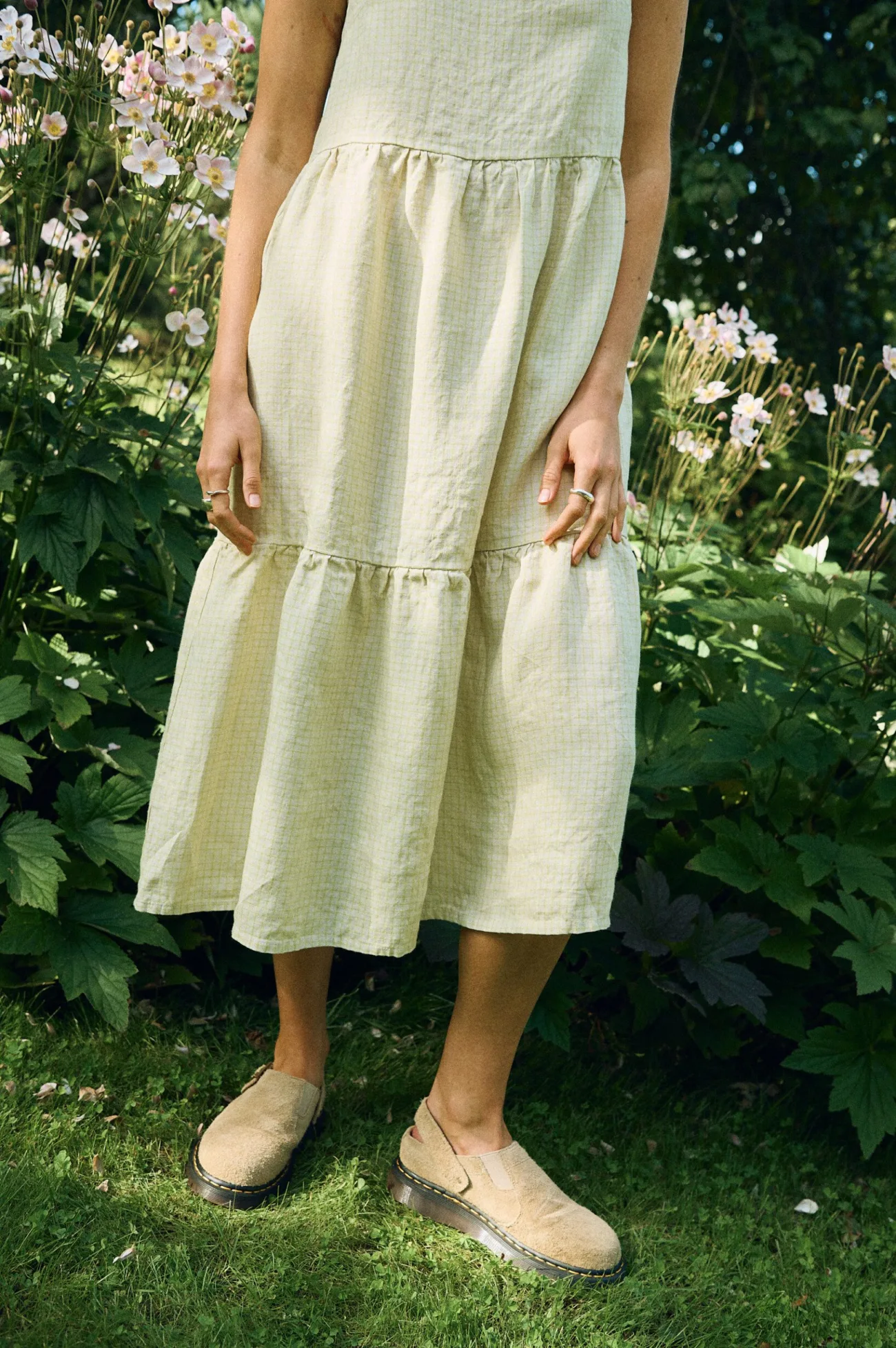 Close-up of a tiered midi dress in apple checks linen, featuring a softly gathered skirt and a relaxed silhouette