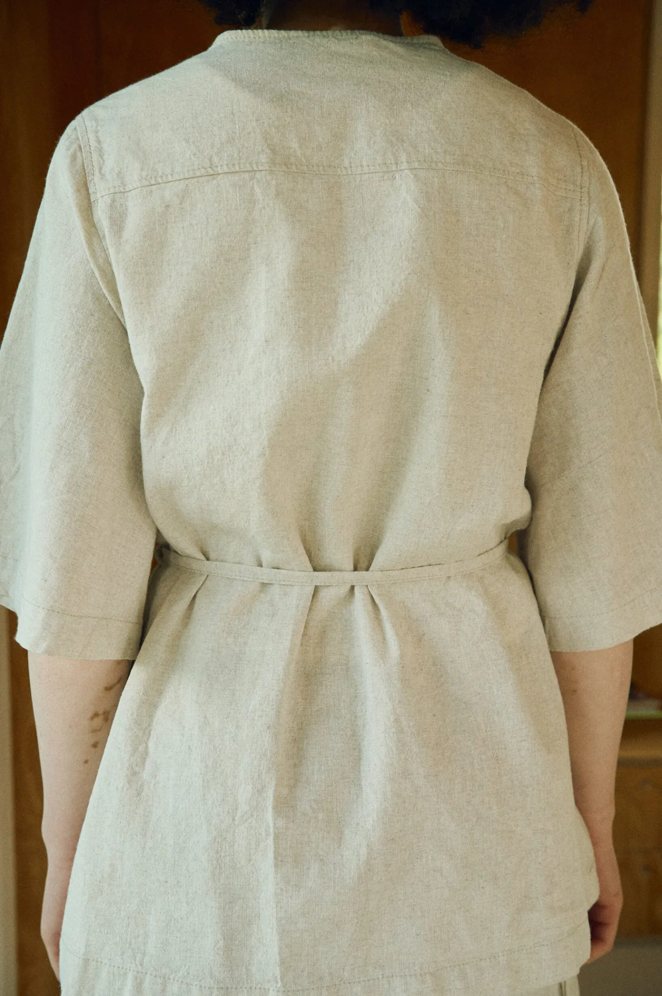 Close-up back view of a natural cotton blend overshirt, highlighting its soft texture, elbow-length sleeves, and a narrow belt cinching the waist