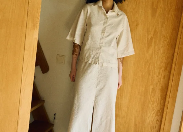 Full front view of a neutral-toned linen-cotton outfit featuring a short-sleeve collared button-up shirt paired with a high-waisted midi skirt with a front slit