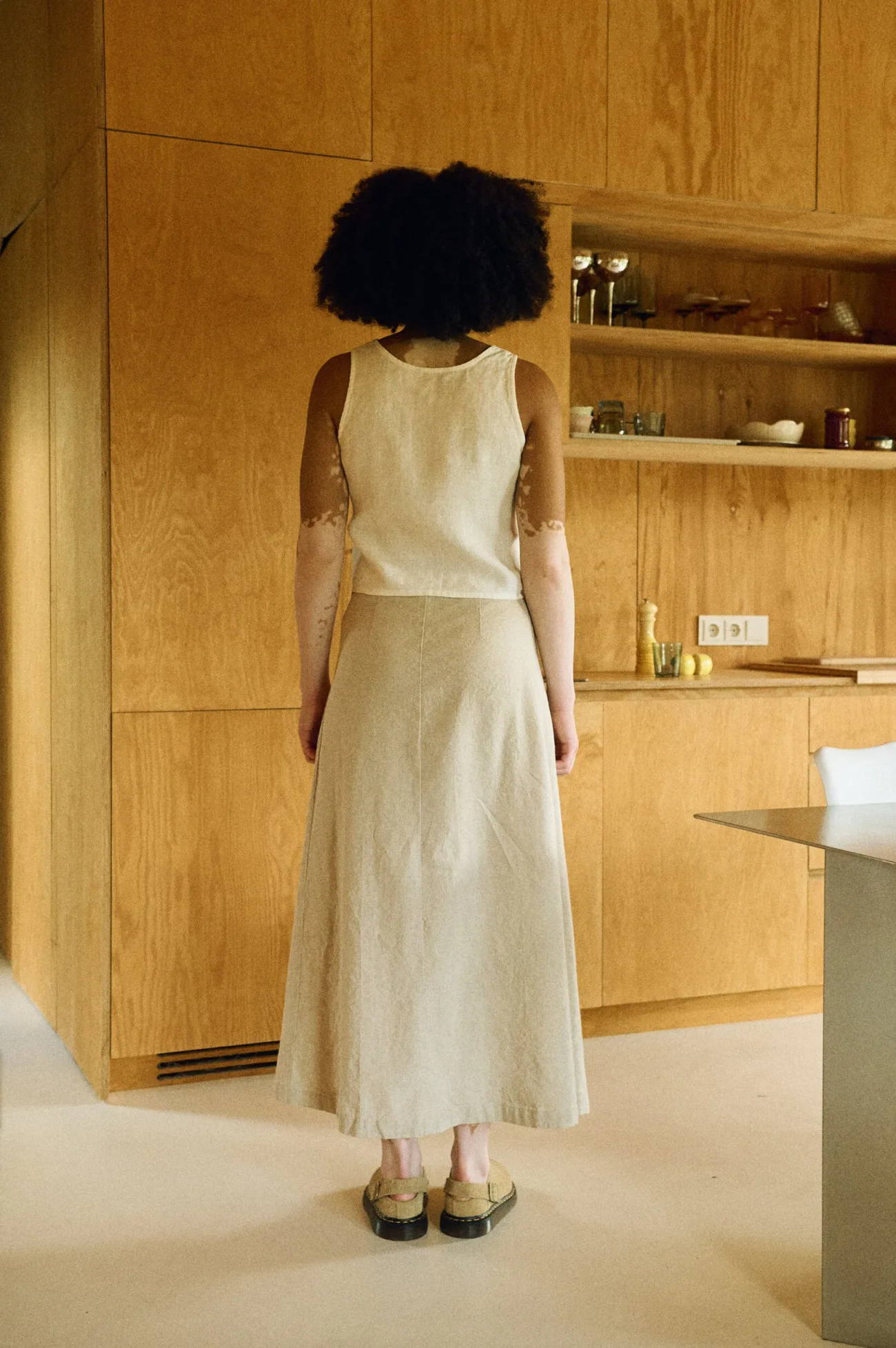 Back view of a woman wearing a sleeveless natural linen top paired with an ankle-length A-line skirt in a cotton-linen blend