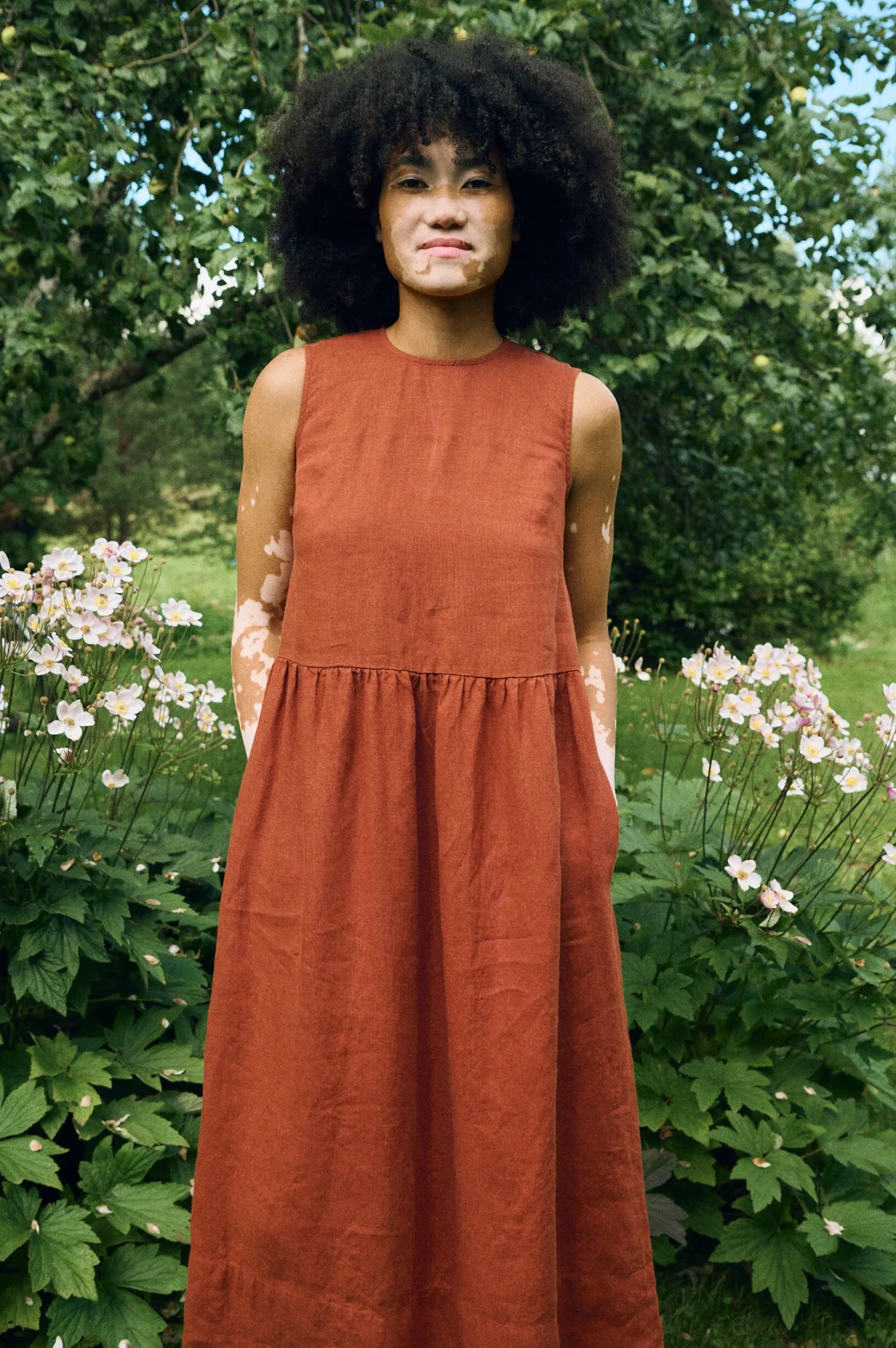 Close-up of a sleeveless terracotta linen dress featuring a high neckline, fitted bodice, gathered waist seam, and side seam pockets