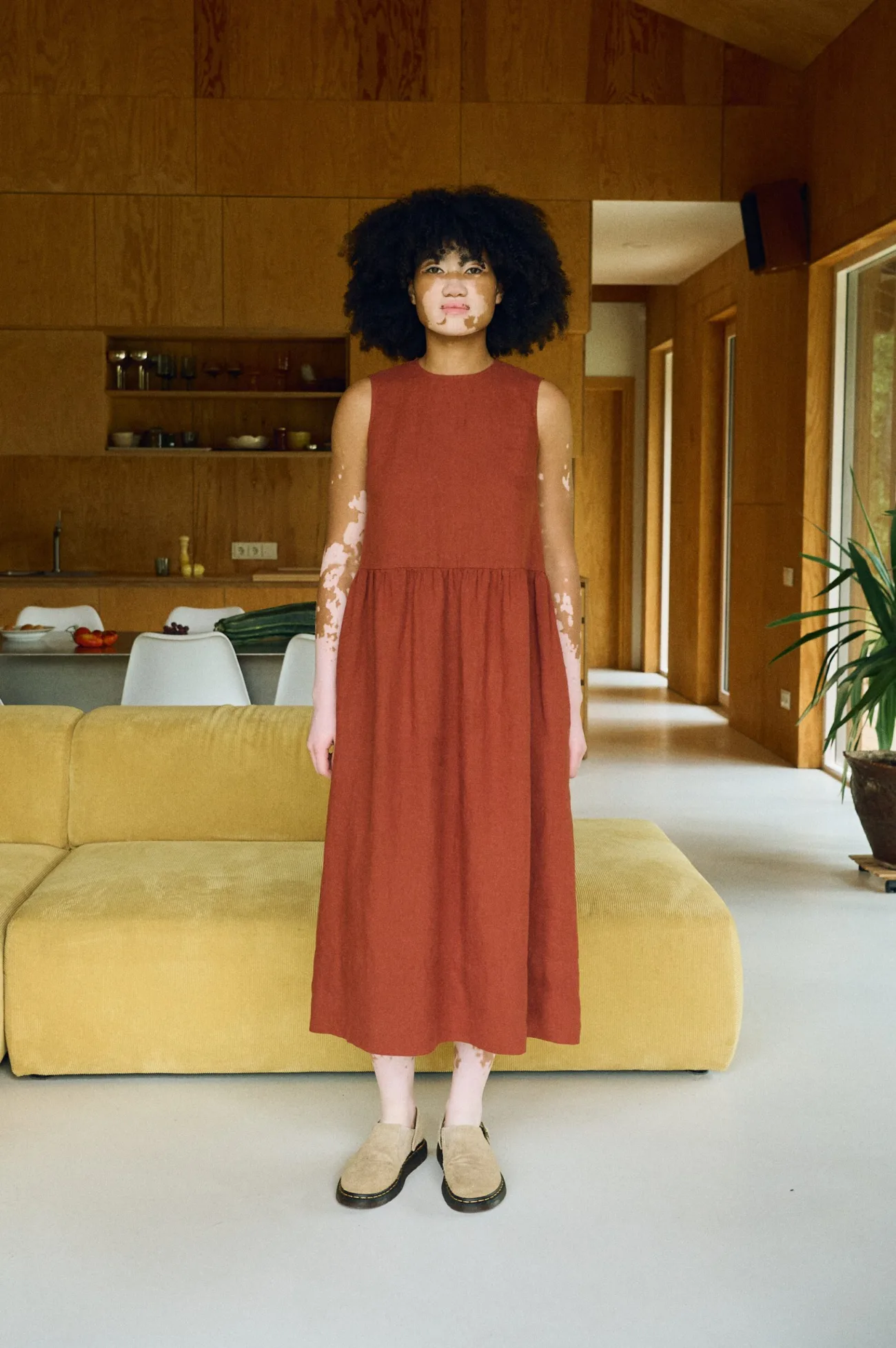 Front-facing view of a sleeveless terracotta linen dress featuring a high neckline, a fitted bodice, a gathered waist seam, and a softly flared midi-length skirt