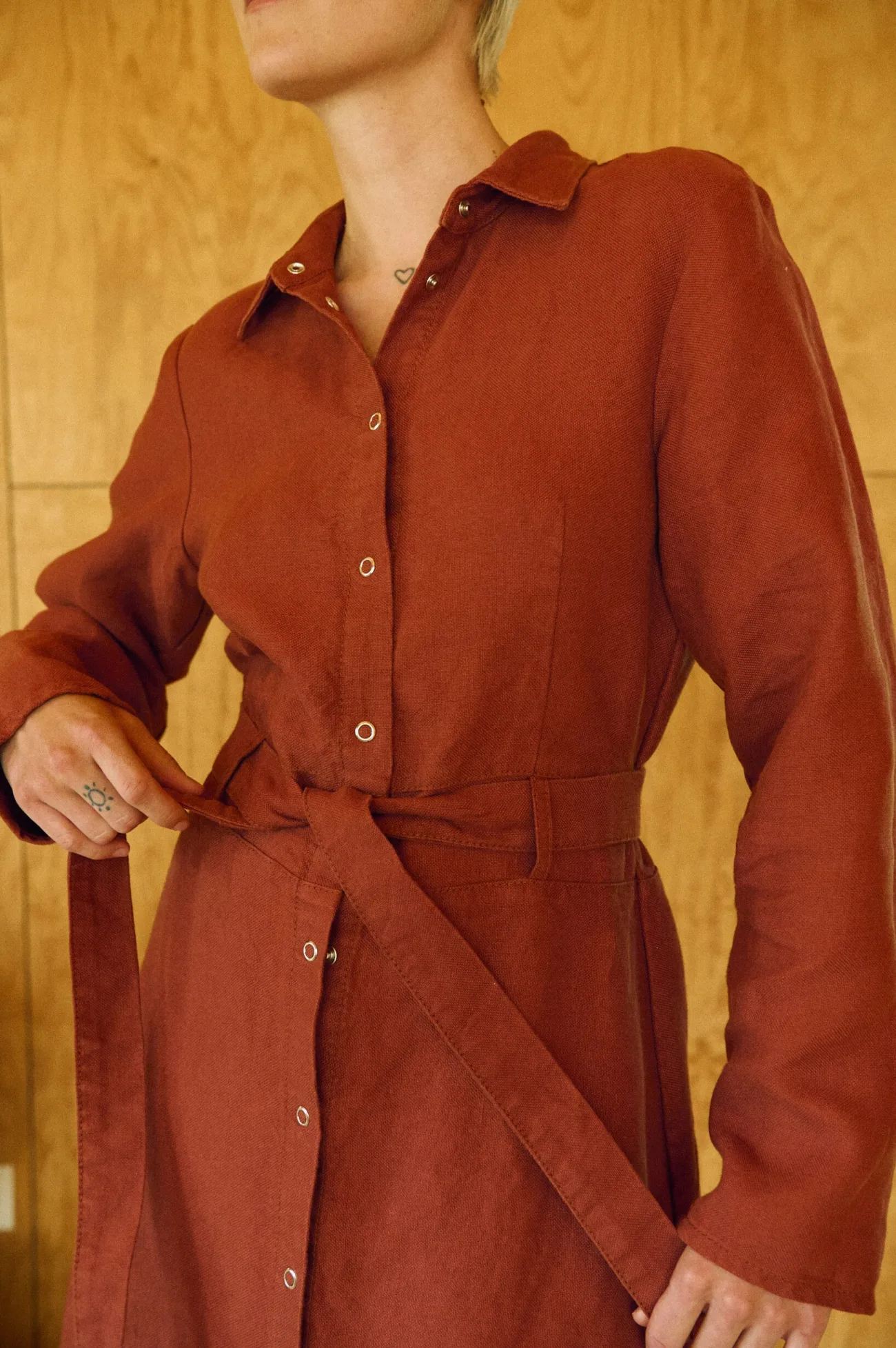 Close-up of terracotta heavy linen dress with collared neck, snap closure, and belt