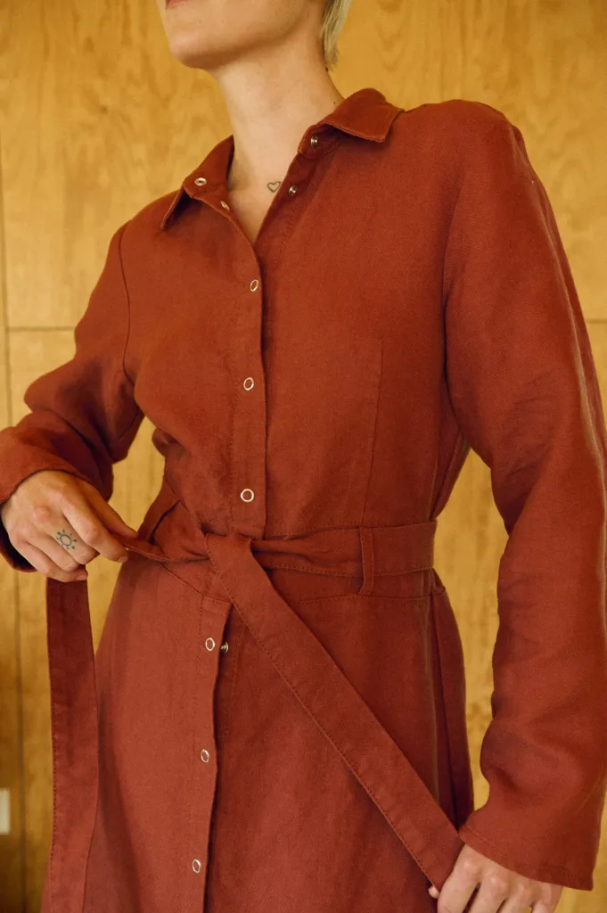 Close-up of terracotta heavy linen dress with collared neck, snap closure, and belt
