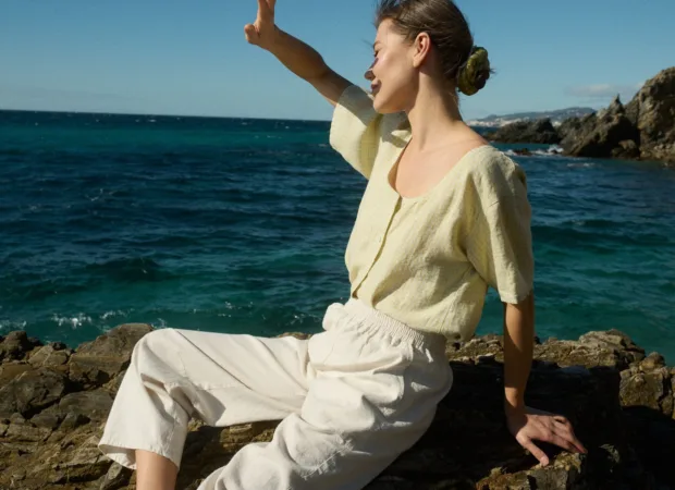 woman in linen clothing sitting by the sea