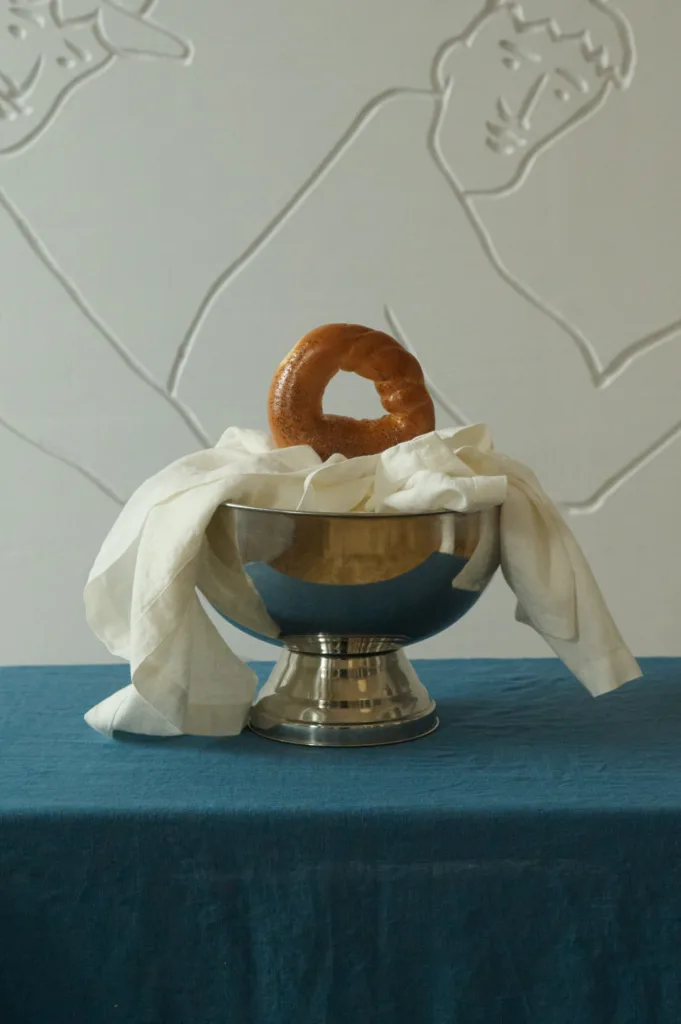 Silver bowl lined with soft milky white linen kitchen towel holding a round bread ring, displayed on a stellar blue linen tablecloth