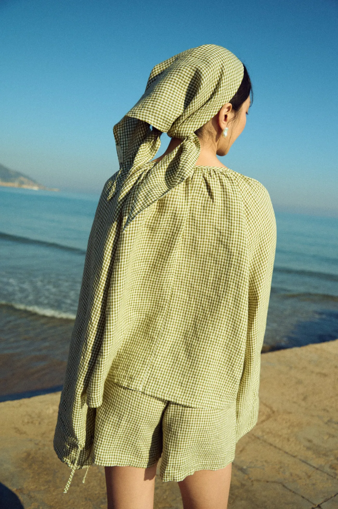 Triangle head wrap in moss green mini gingham linen worn with a lightweight gathered blouse and coordinating shorts