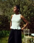 White linen smocked sleeveless top with gathered texture and ruffled hem, paired with black linen culottes