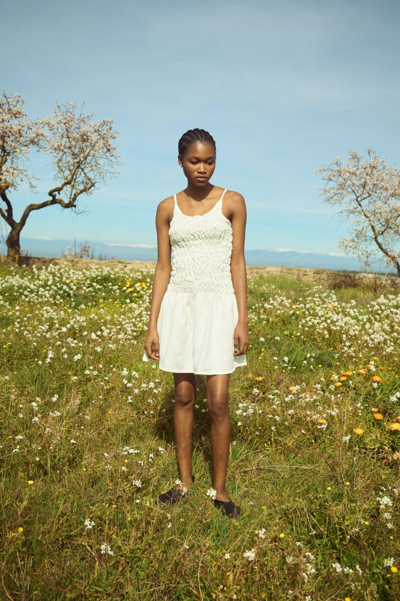 Milky white linen mini dress with thin straps, a ruched smocked bodice, and a softly flared skirt