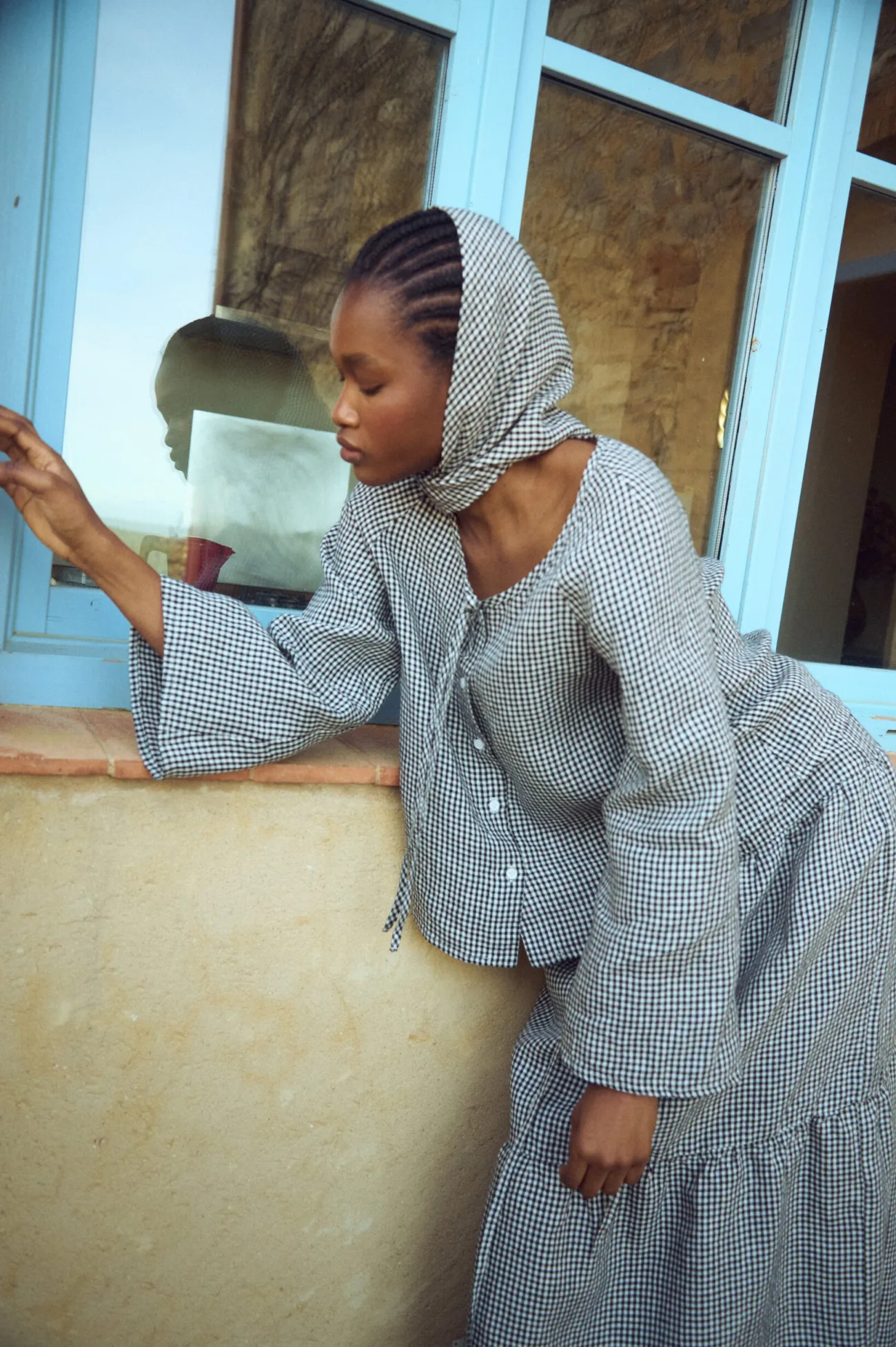 Side view of a black mini gingham linen blouse with buttons and wide sleeves paired with a matching gingham headscarf and tiered skirt