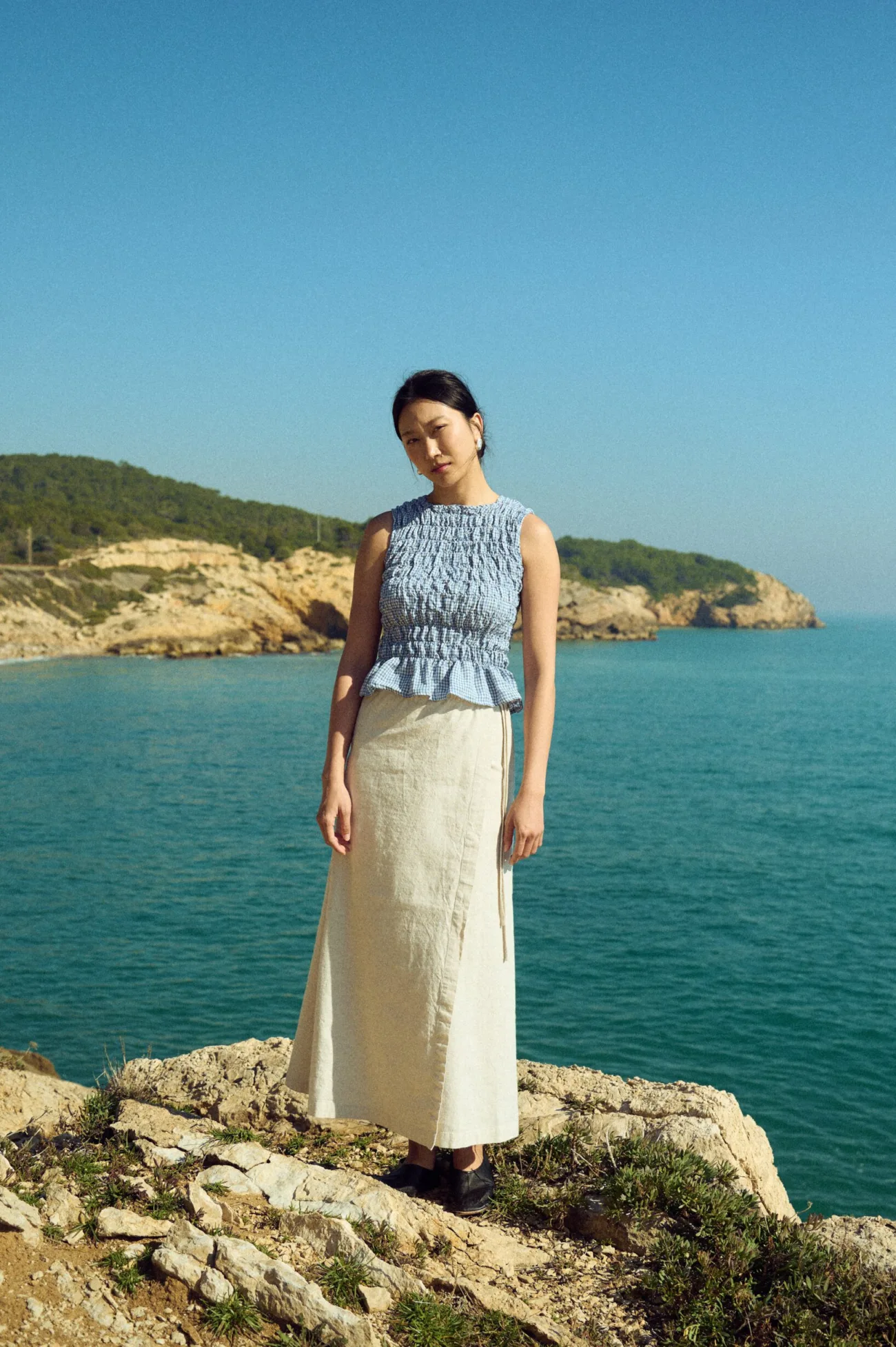 Lightweight linen top in blue gingham featuring all-over elasticated smocking and a soft peplum finish, paired with a neutral linen cotton blend skirt