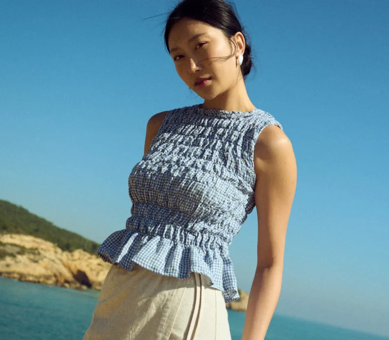 Blue gingham linen smocked top with gathered texture and soft peplum hem, paired with a natural linen cotton blend wrap skirt