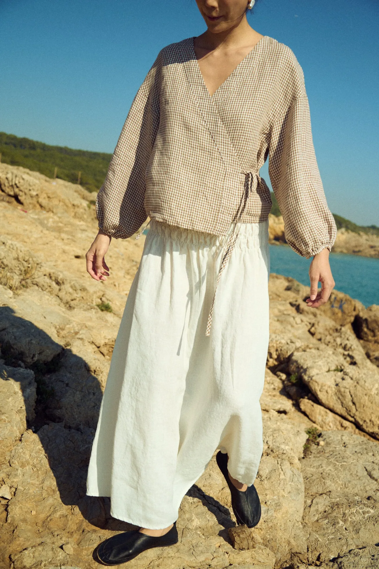 Soft brown gingham linen wrap top with subtle volume through the sleeves and a tied waist, paired with a white linen skirt