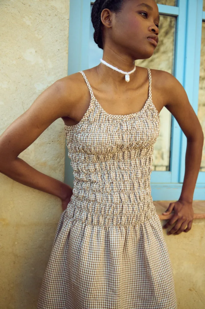 Model wearing a brown gingham linen dress with a smocked bodice and thin straps