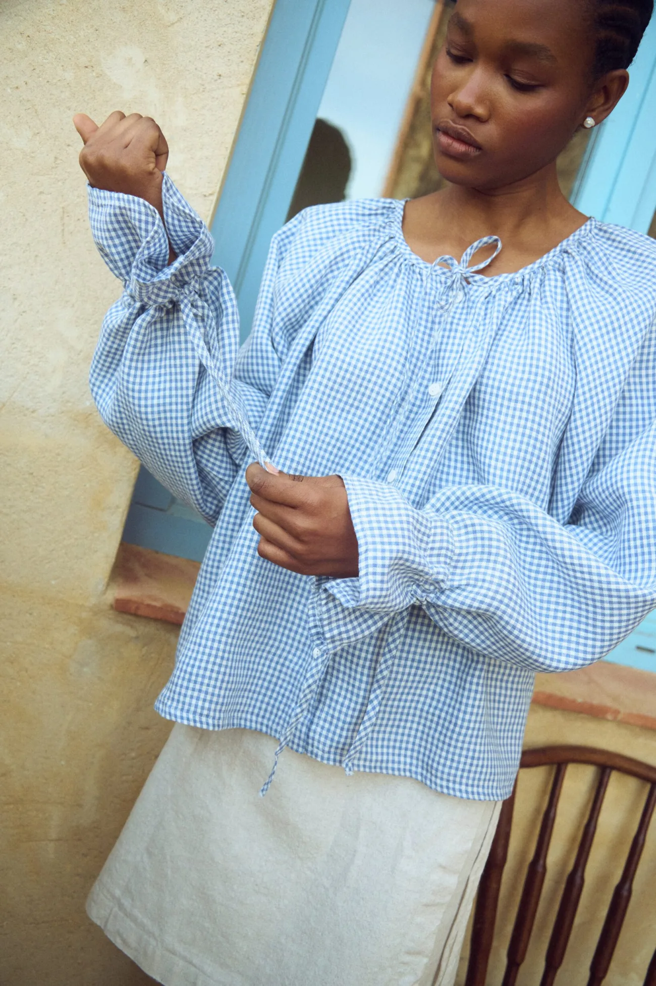 Blue gingham linen top with gathered neckline, button front and adjustable tie sleeves, paired with a linen mini skirt