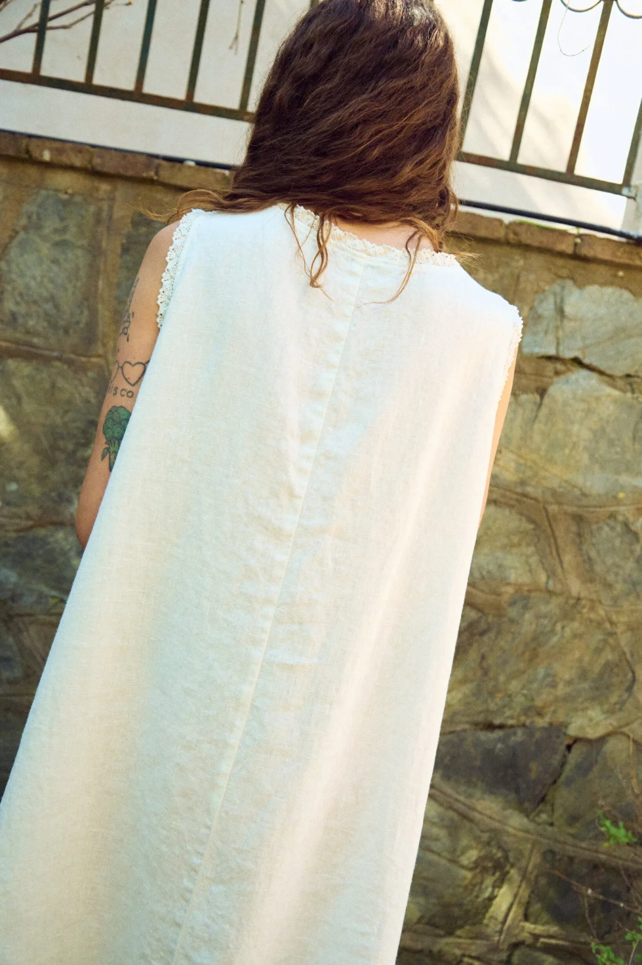 Close back view of milky white linen sleeveless midi dress with lace-trim neckline, center seam, and loose drape
