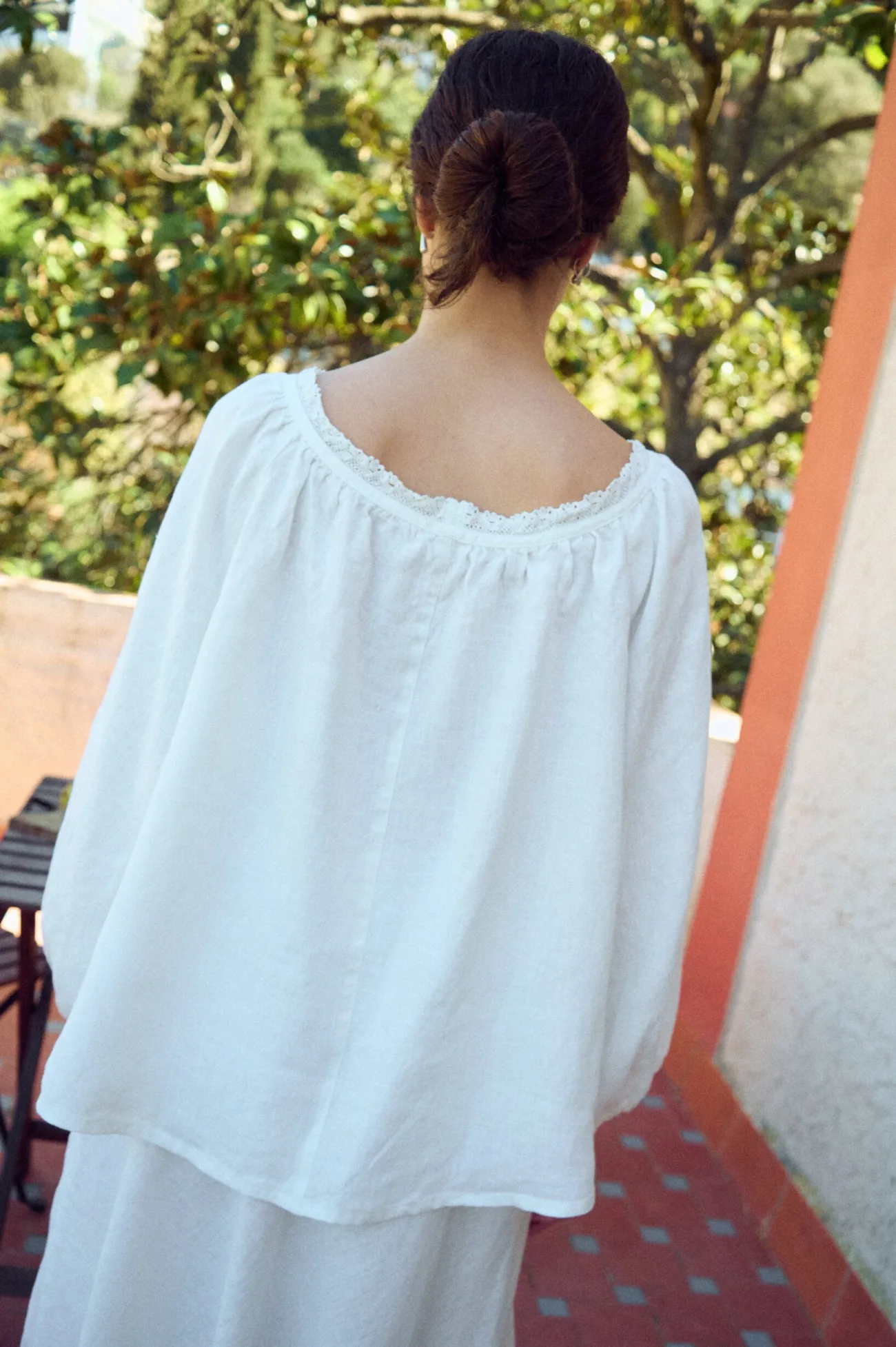 Back view of milky white linen blouse with lace-trim scoop neckline, long sleeves, and a loose, airy silhouette