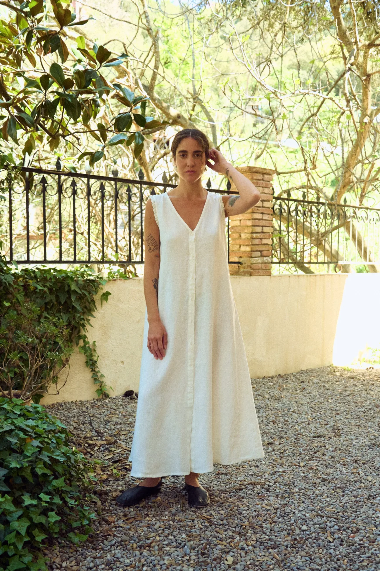 A relaxed white linen dress with a sleeveless cut, soft V-neckline and full button front, falling into a gently flared, ankle-grazing silhouette