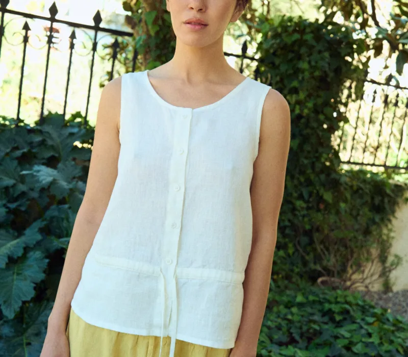 White sleeveless linen top with a relaxed fit, round neckline, button-front closure, and subtle waist seam with tie detail