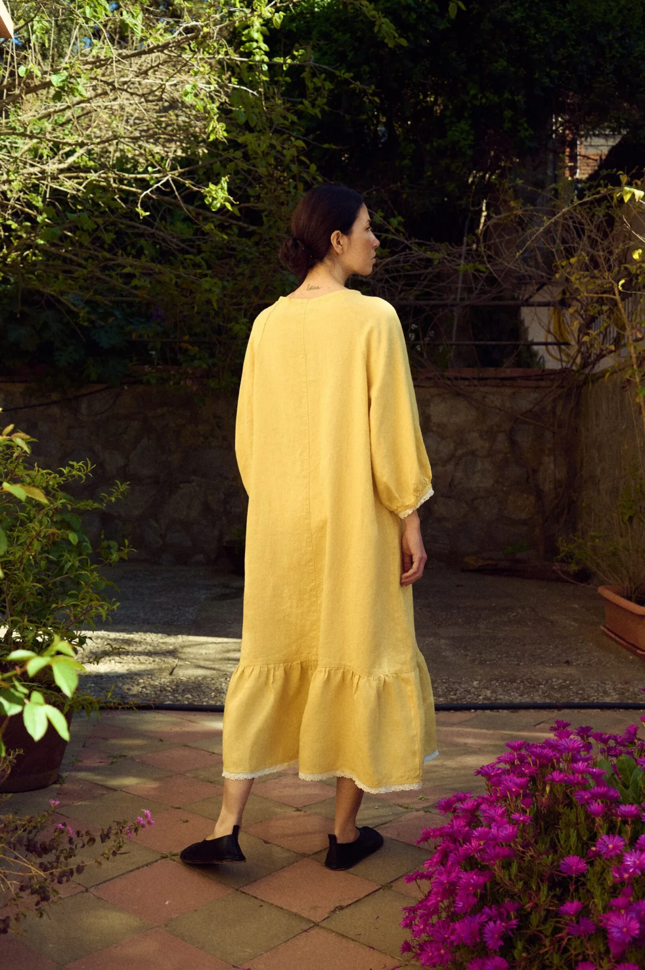 Yellow linen dress with a relaxed A-line drape, round neckline, softly gathered three-quarter sleeves with lace-trimmed cuffs, and a tiered hem finished with delicate lace detailing