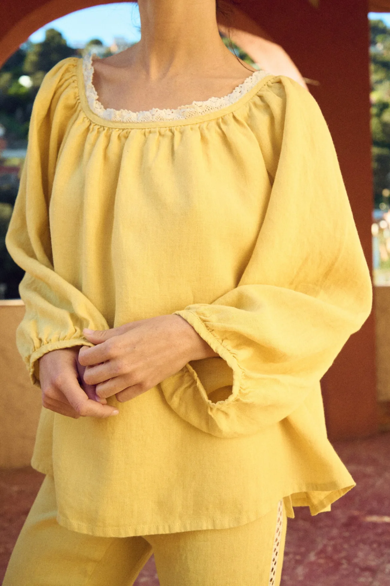 Close-up of butter yellow linen blouse with lace-trimmed scoop neckline, soft gathered front, and voluminous sleeves